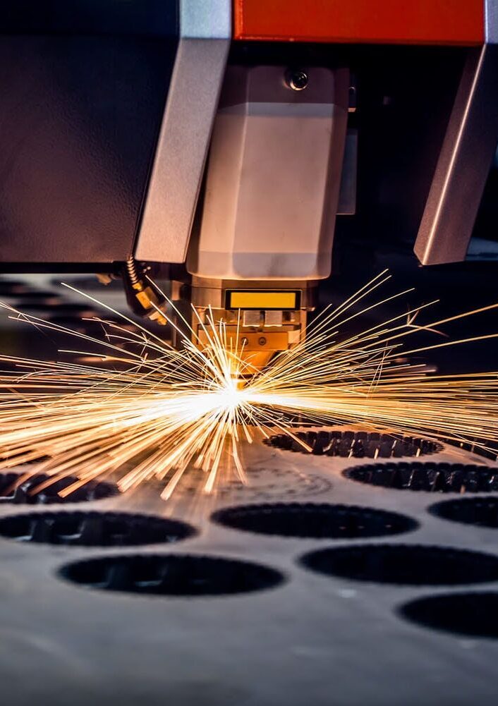 Řezací hlava laseru a sršící jiskry při řezání otvorů do plechu